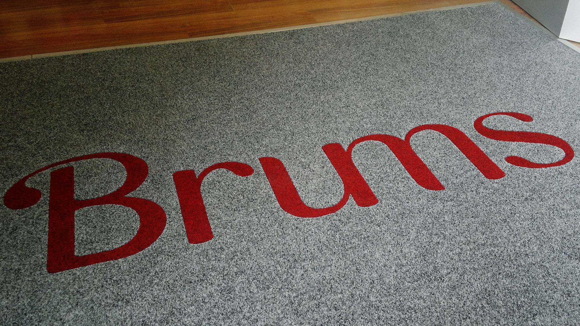 Ingresso di un negozio con un Tappeto intarsiato personalizzato con il logo Brums di colore grigio e Rosso